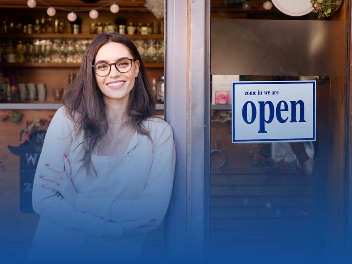 A woman smiling outside her open shop. Vanmark can help you with commercial mortgages.