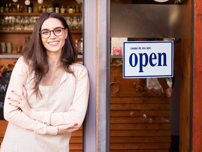 A woman smiling outside her open shop.